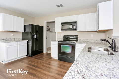 A kitchen with a black fridge and stove, white cabinets, and a granite countertop.
