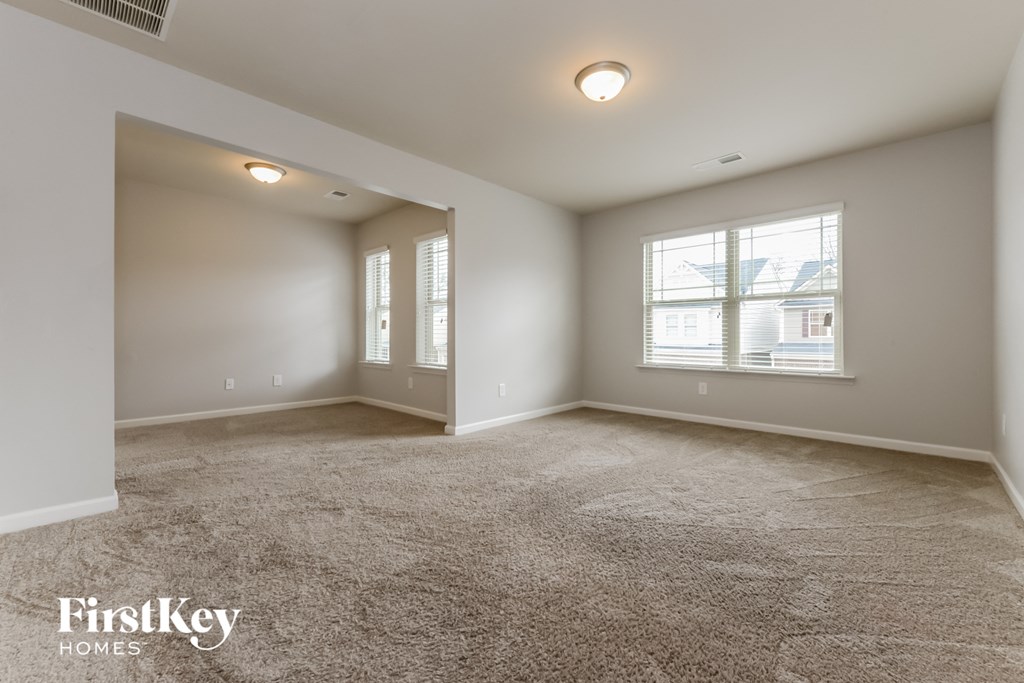 A spacious room with a carpeted floor and a window with blinds.
