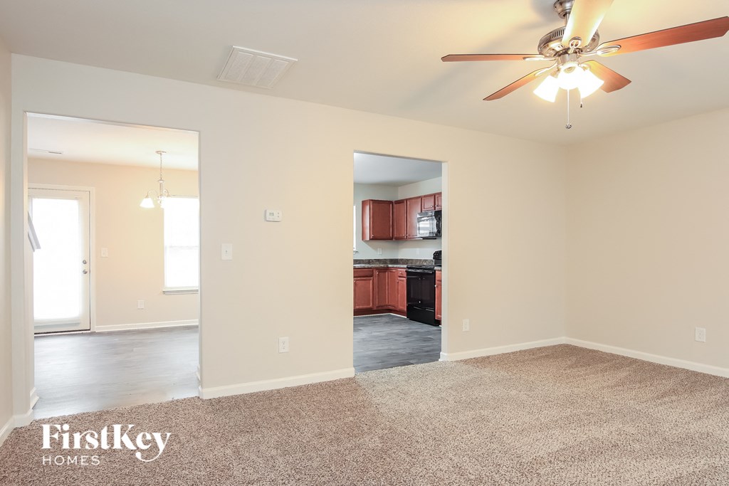 a empty living room with a ceiling fan and a kitchen
