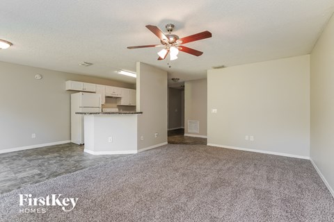 an empty living room with a ceiling fan and a kitchen