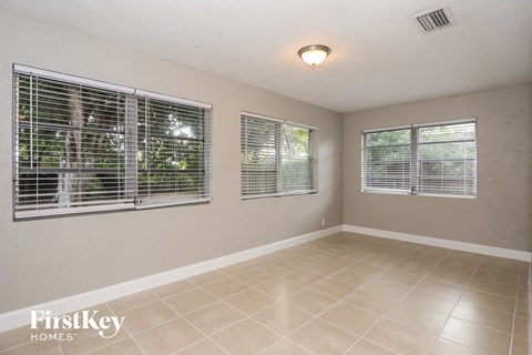 A room with beige walls and tiled flooring, with three windows covered in blinds.