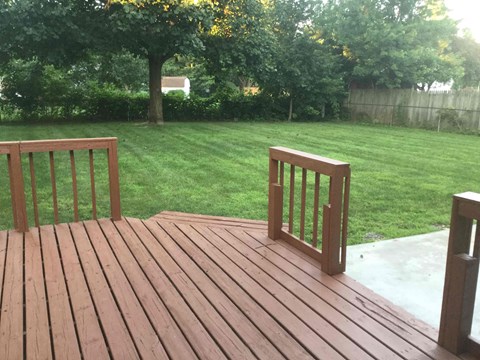 a backyard with a wooden deck and a lawn and trees