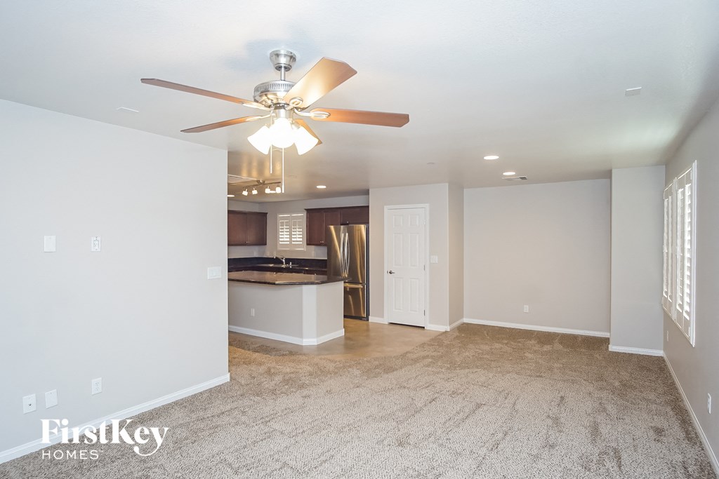 an empty living room with a ceiling fan and a kitchen