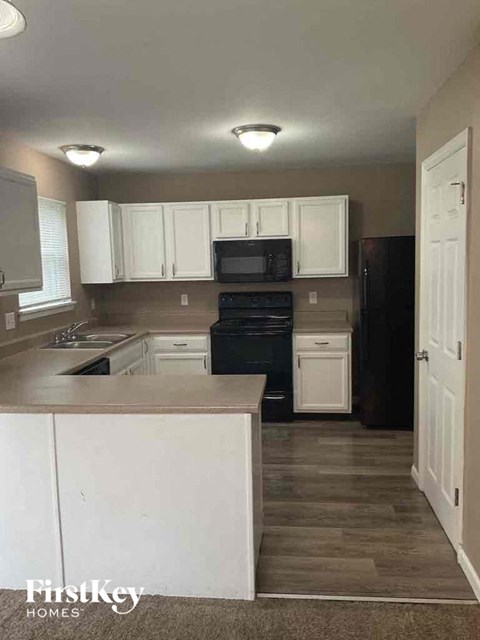 A kitchen with white cabinets and a black refrigerator.
