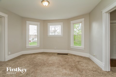 A room with beige carpet and three windows.