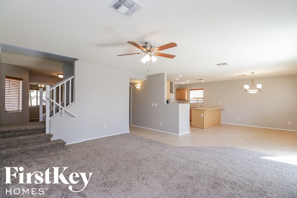 an empty living room with a ceiling fan and a kitchen