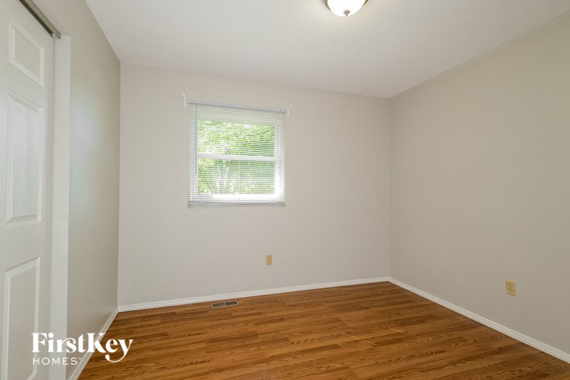 a bedroom with white walls and wood floors and a window