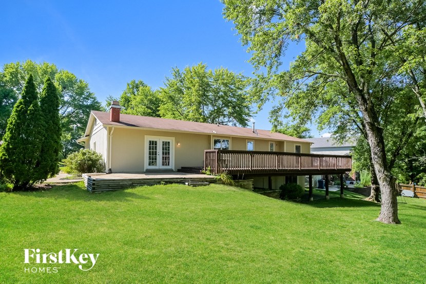 a large yellow house with a deck and a green lawn and trees