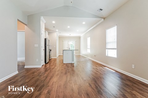 A spacious room with wooden floors and a kitchen area in the background.