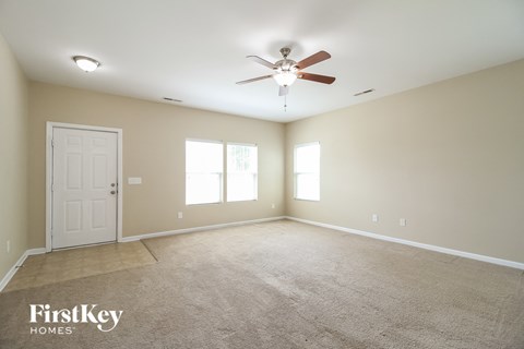 A spacious room with a carpeted floor, a ceiling fan, and a door.