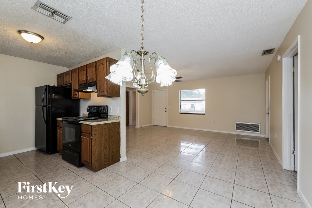 A kitchen area with a black fridge and microwave, wooden cabinets, and a chandelier hanging from the ceiling.