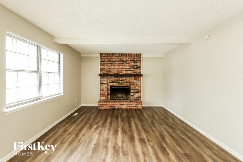an empty living room with a brick fireplace and wooden floors