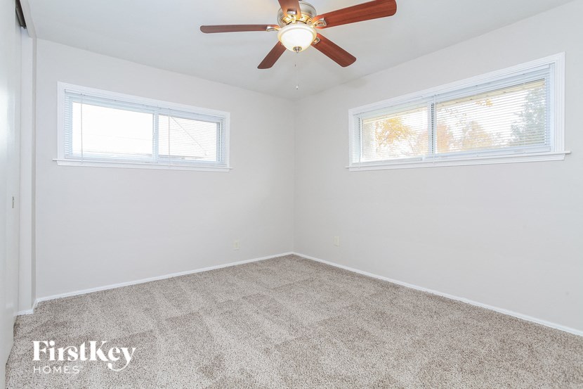 an empty bedroom with a ceiling fan and two windows