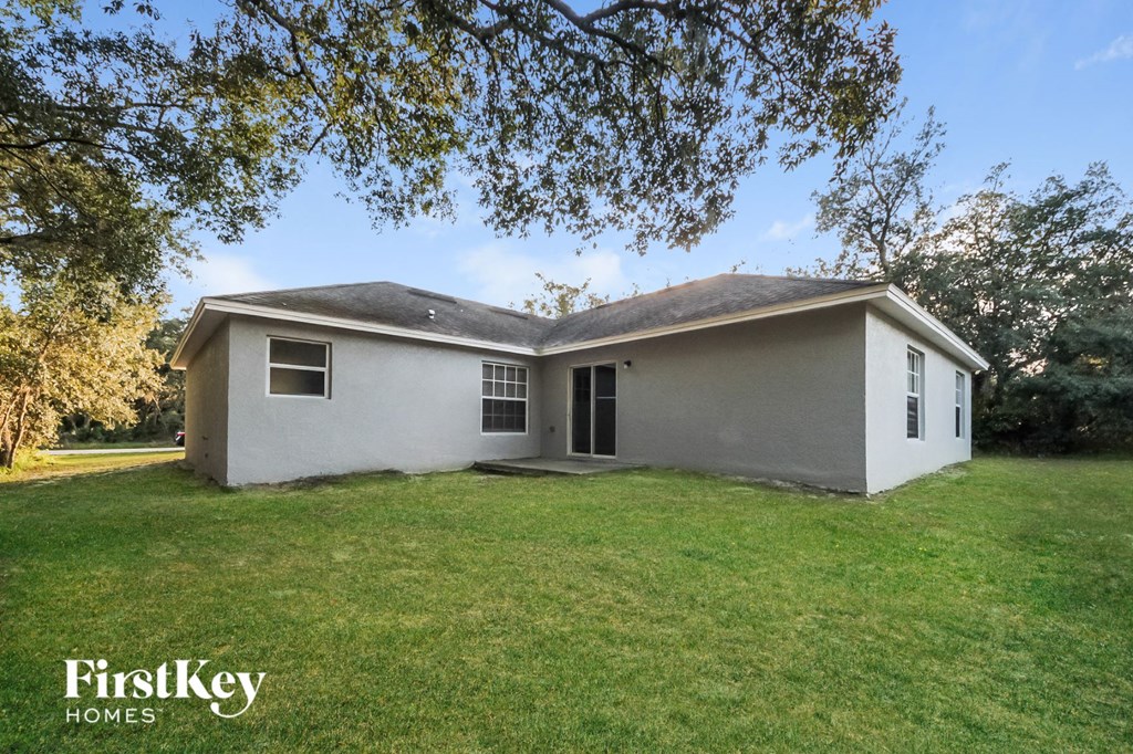 A house with a white exterior and a black roof is surrounded by a grassy lawn.