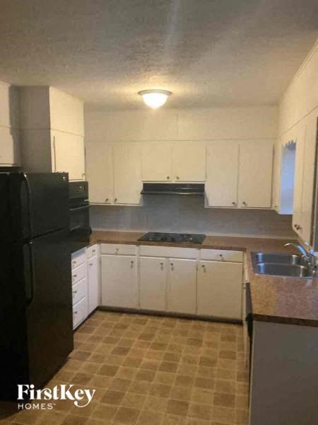 A kitchen with white cabinets and a black refrigerator.