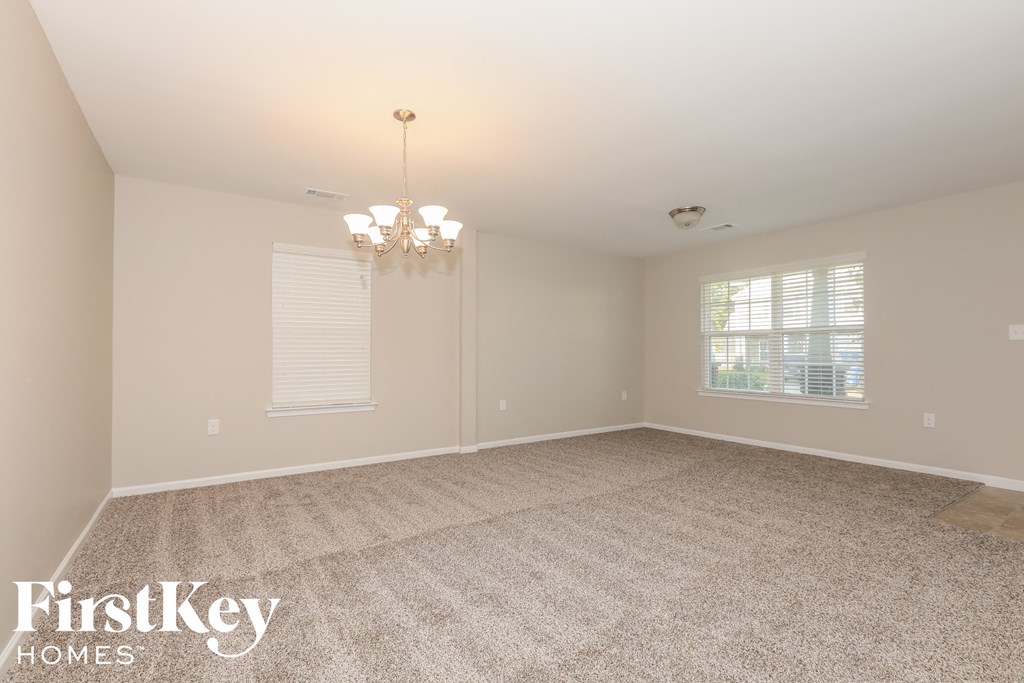 A spacious room with a chandelier and a window with blinds.
