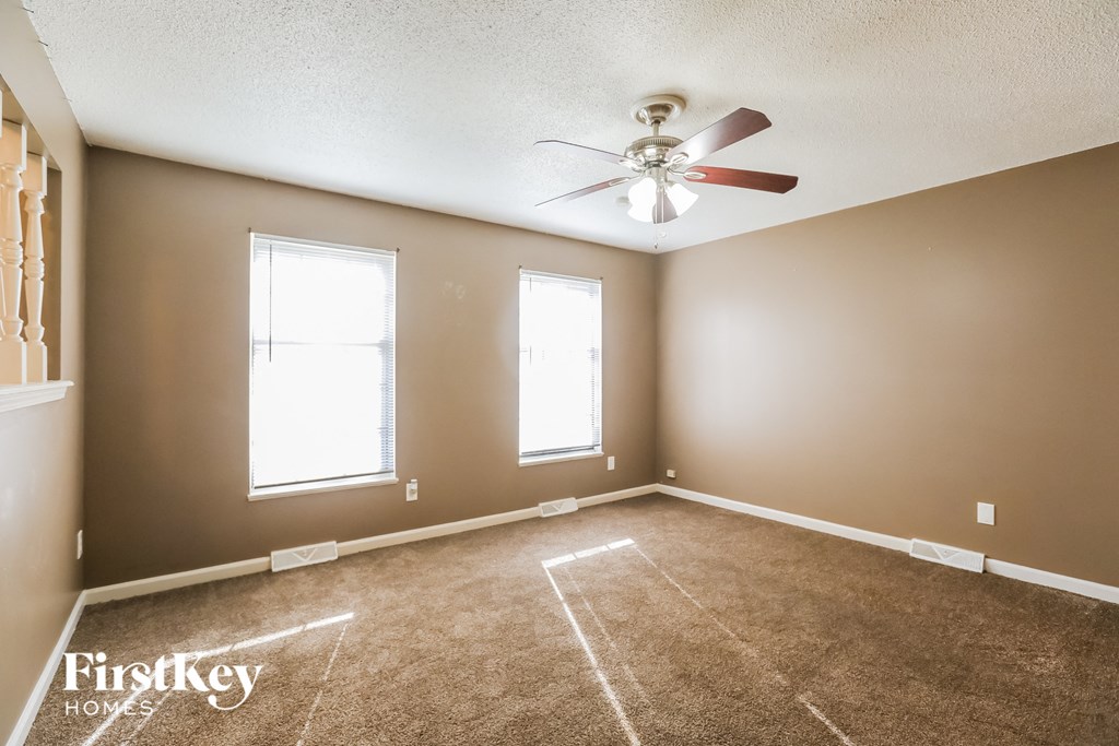 an empty living room with a ceiling fan and two windows