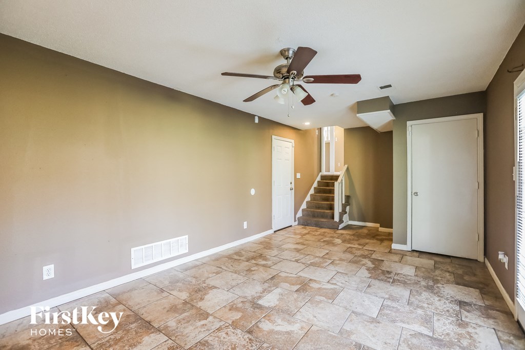 an empty living room with a ceiling fan and a staircase