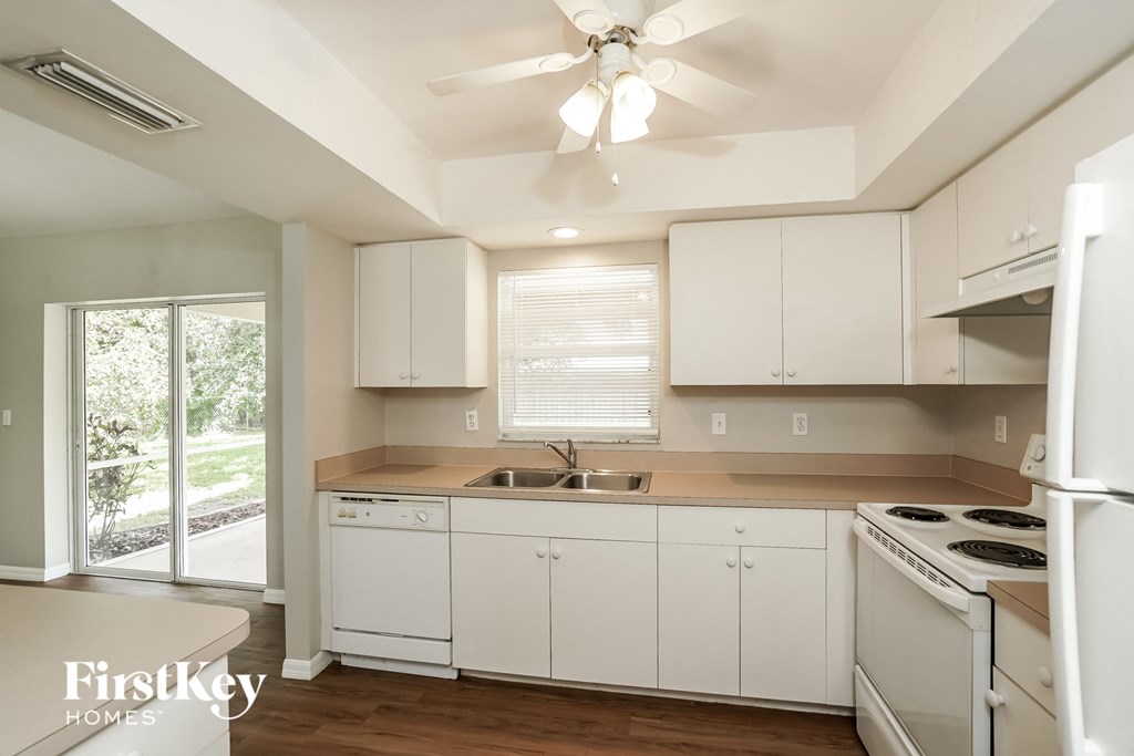 a kitchen with white cabinets and white appliances and a ceiling fan
