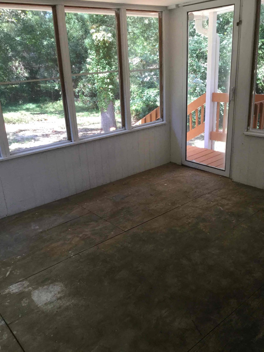 A room with a concrete floor and a view of trees through the windows.