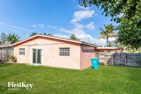 A small house with a pinkish exterior is shown with a green trash can in front of it.
