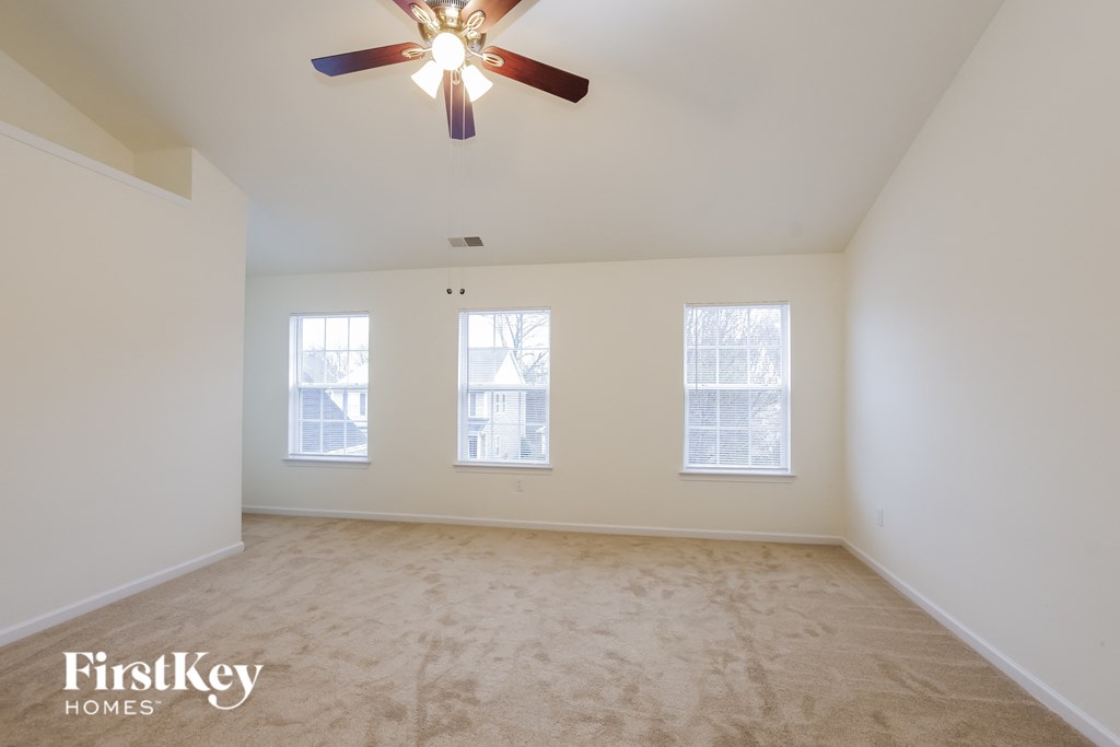 A spacious room with a ceiling fan and two windows.