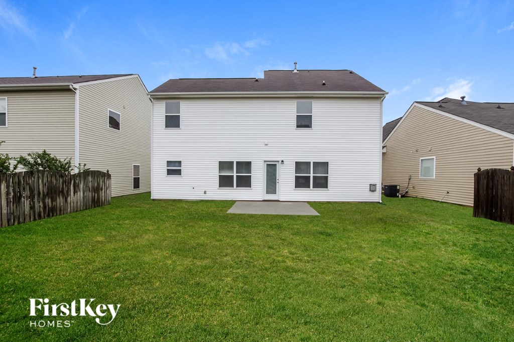 A white house with a brown roof is surrounded by a fence and has a grassy yard.