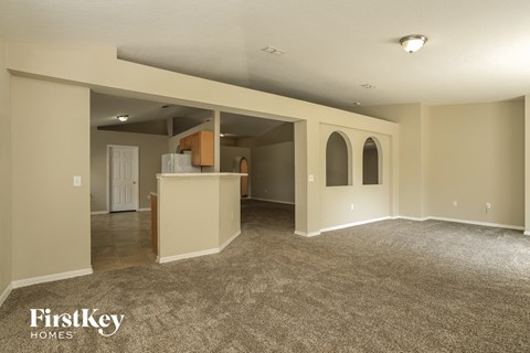 A spacious room with a carpeted floor and a kitchen area in the background.