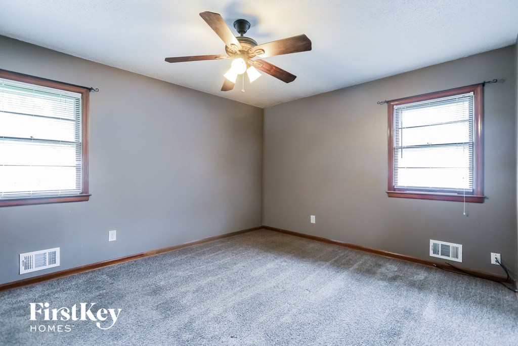 an empty room with a ceiling fan and two windows