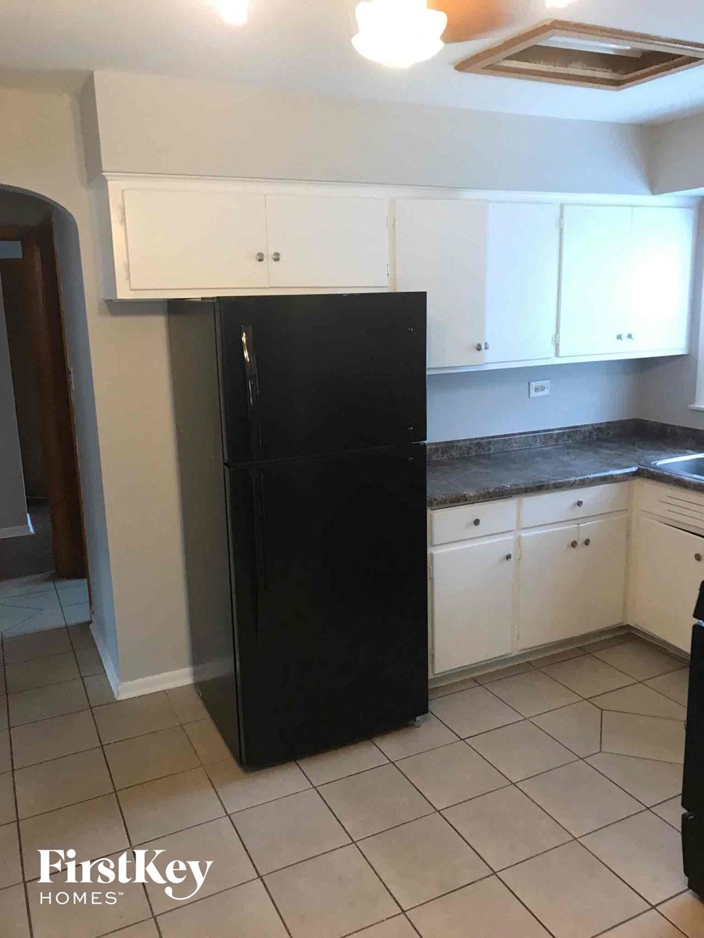 a black refrigerator in a kitchen with white cabinets
