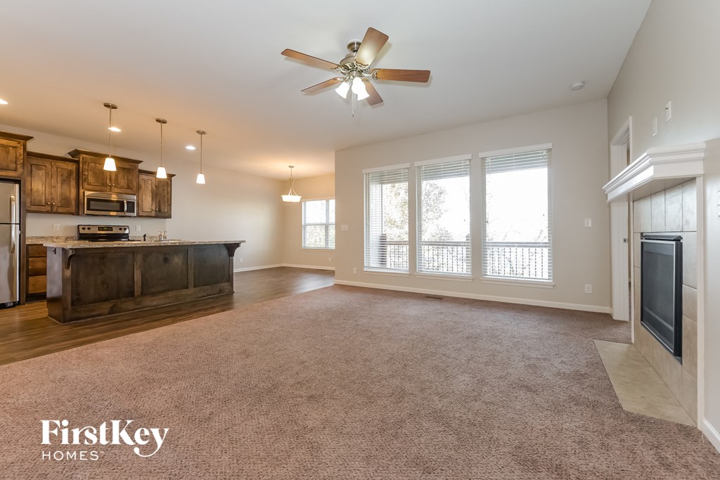 an empty living room with a kitchen and a ceiling fan