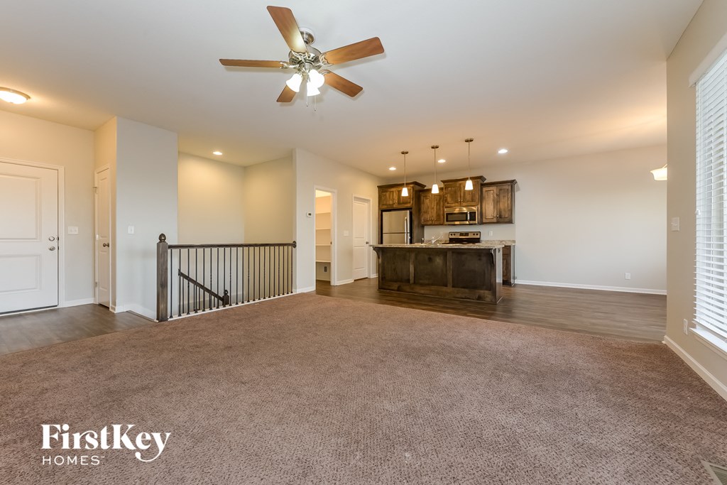 an empty living room with a ceiling fan and a kitchen