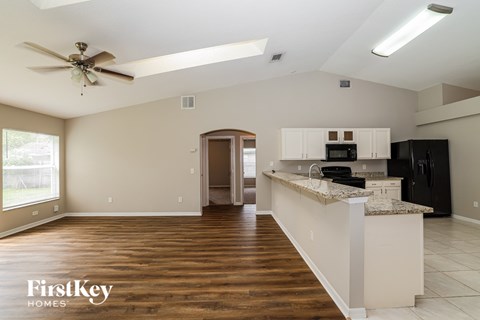 A spacious kitchen and living room with a wood floor and a ceiling fan.