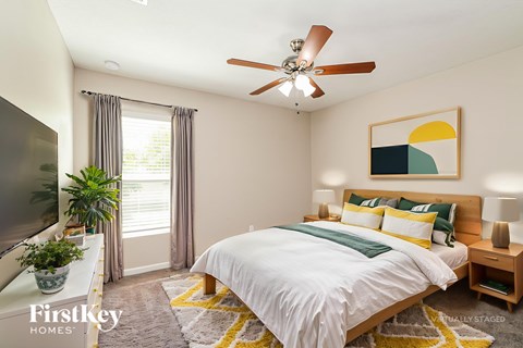A bedroom with a bed, a ceiling fan, and a painting on the wall.