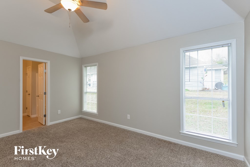 A room with a carpet floor, a ceiling fan, and a window with blinds.
