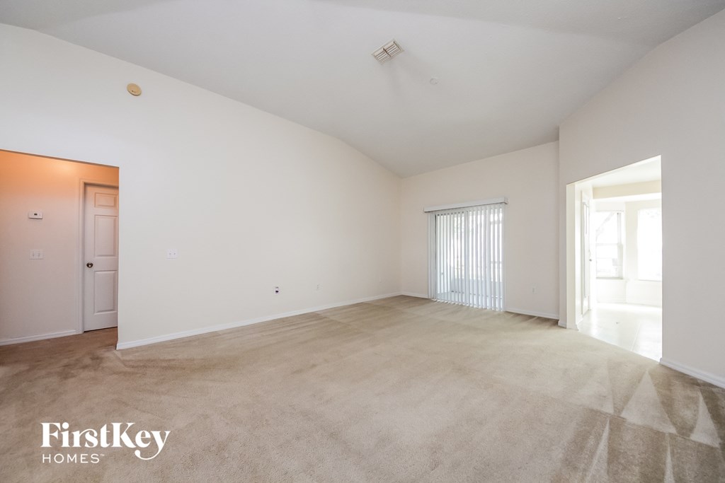 the living room and dining room of an apartment with white walls and carpet