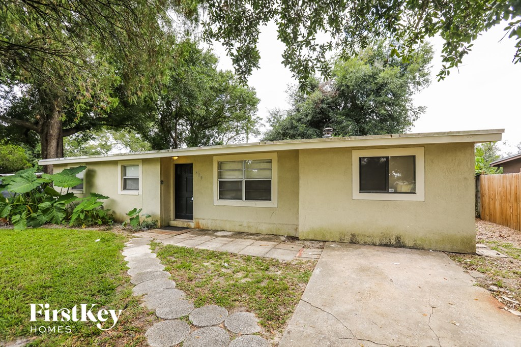 a small tan house with a sidewalk and trees