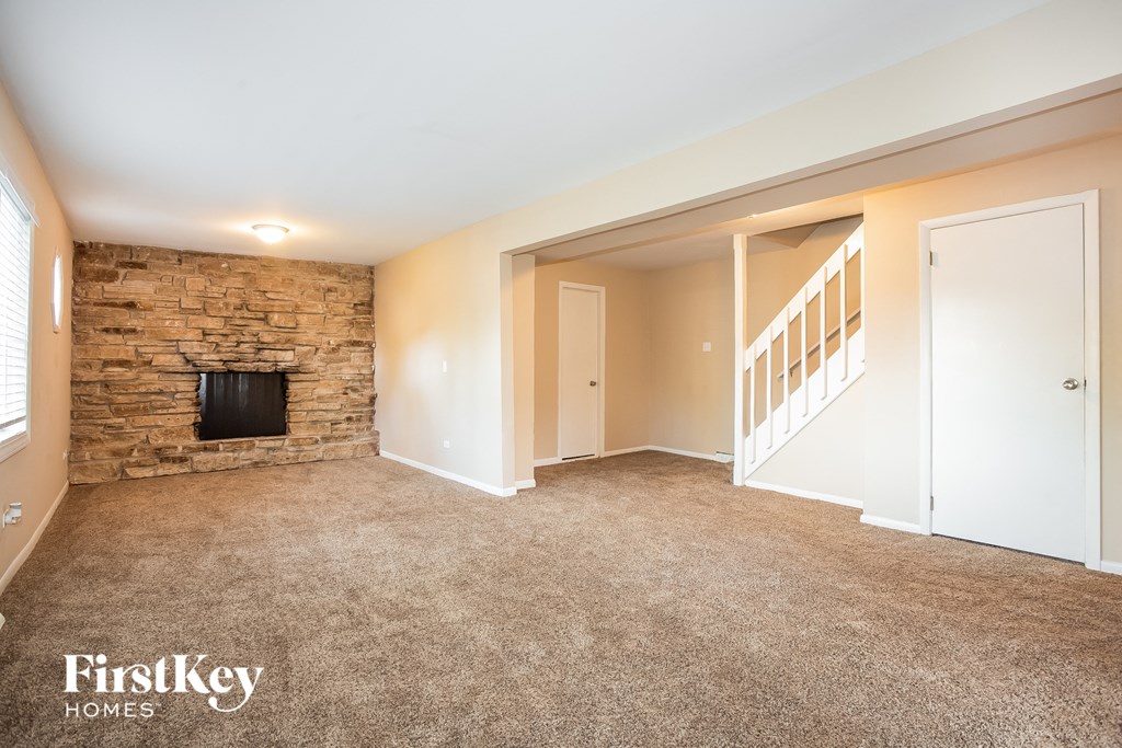 a carpeted living room with a stone fireplace     and a staircase