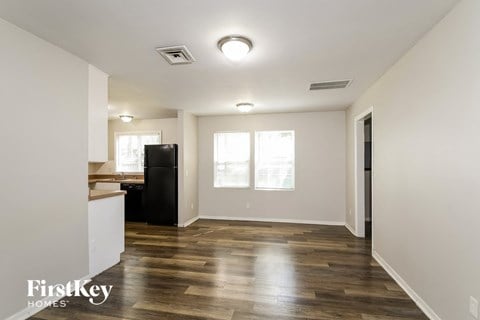 A spacious room with wooden flooring and a black refrigerator.