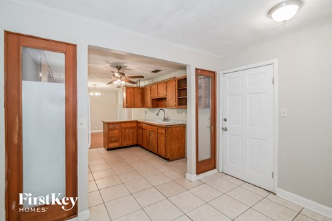 a kitchen with wooden cabinets and a white tile floor and a door to a kitchen