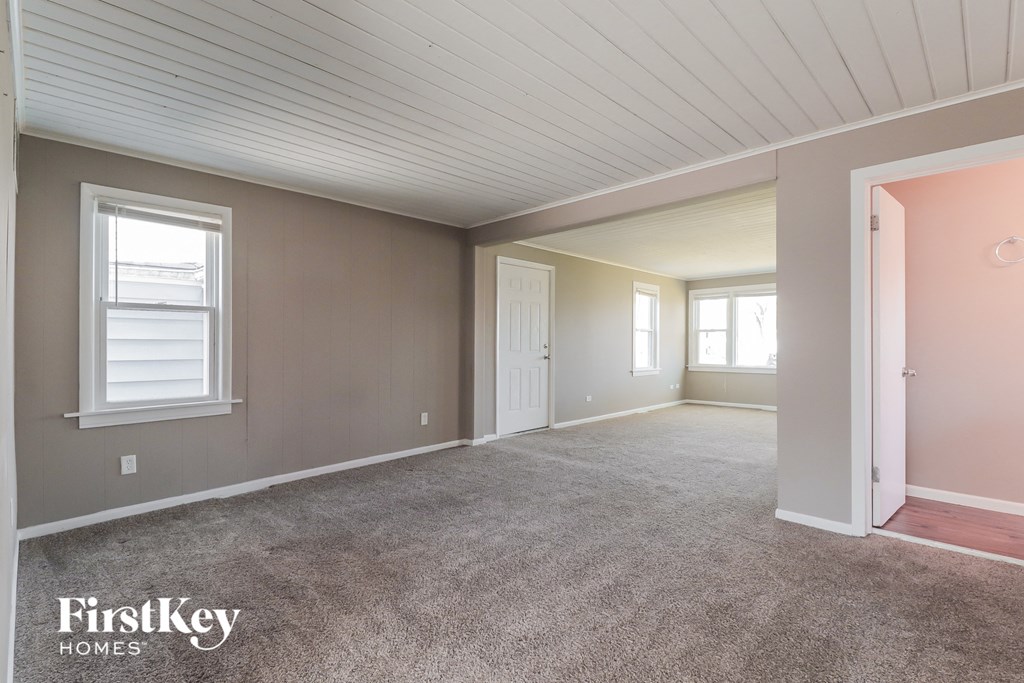 A spacious room with a carpeted floor and a window on the left wall.