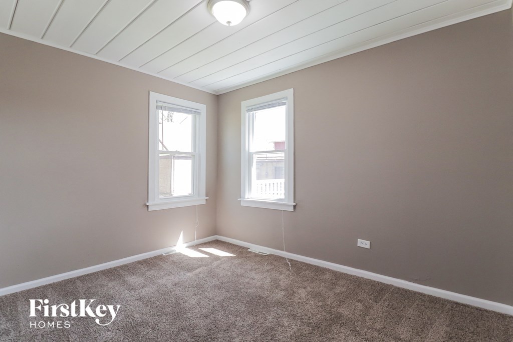 A room with a carpet floor and two windows.