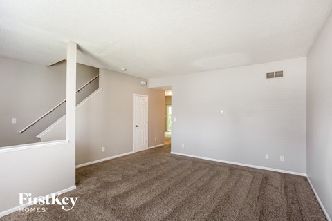 A spacious room with a carpeted floor and a staircase on the left side.