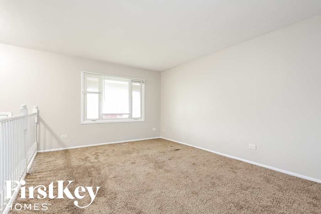 A carpeted room with a window and a white wall.