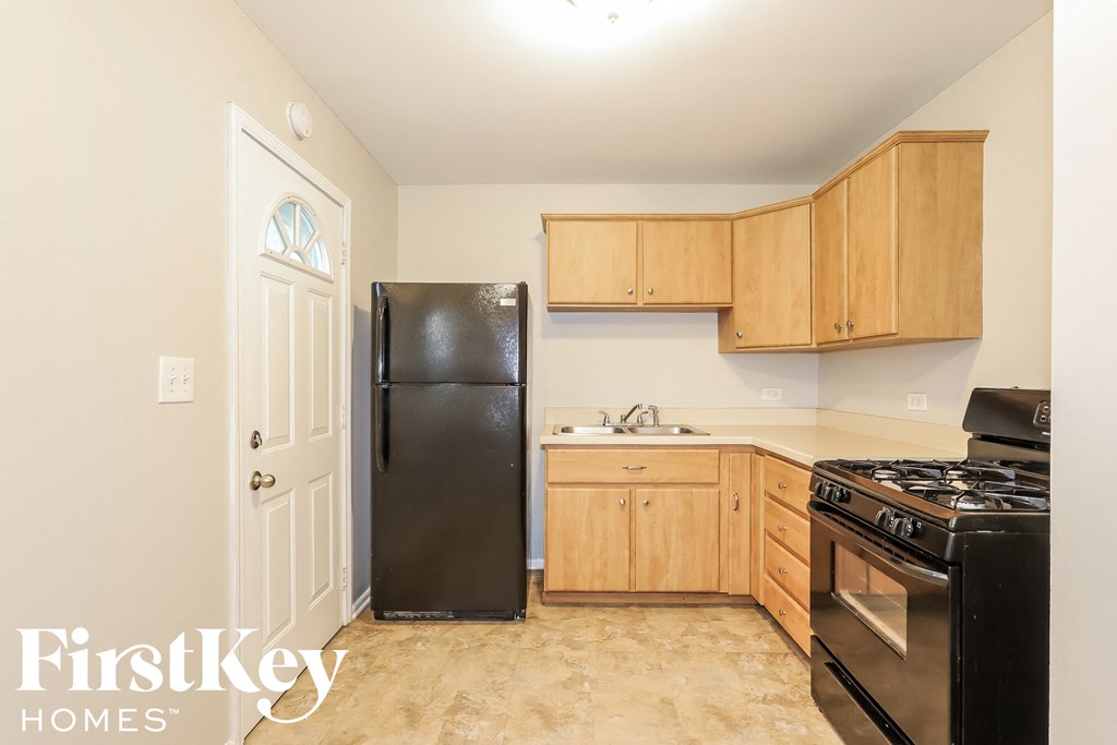 A kitchen with a black fridge, black stove, wooden cabinets and a white door.