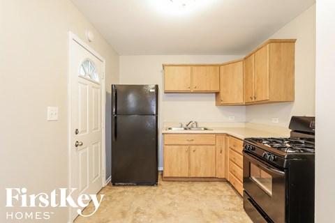 A kitchen with a black fridge, black stove, wooden cabinets and a white door.