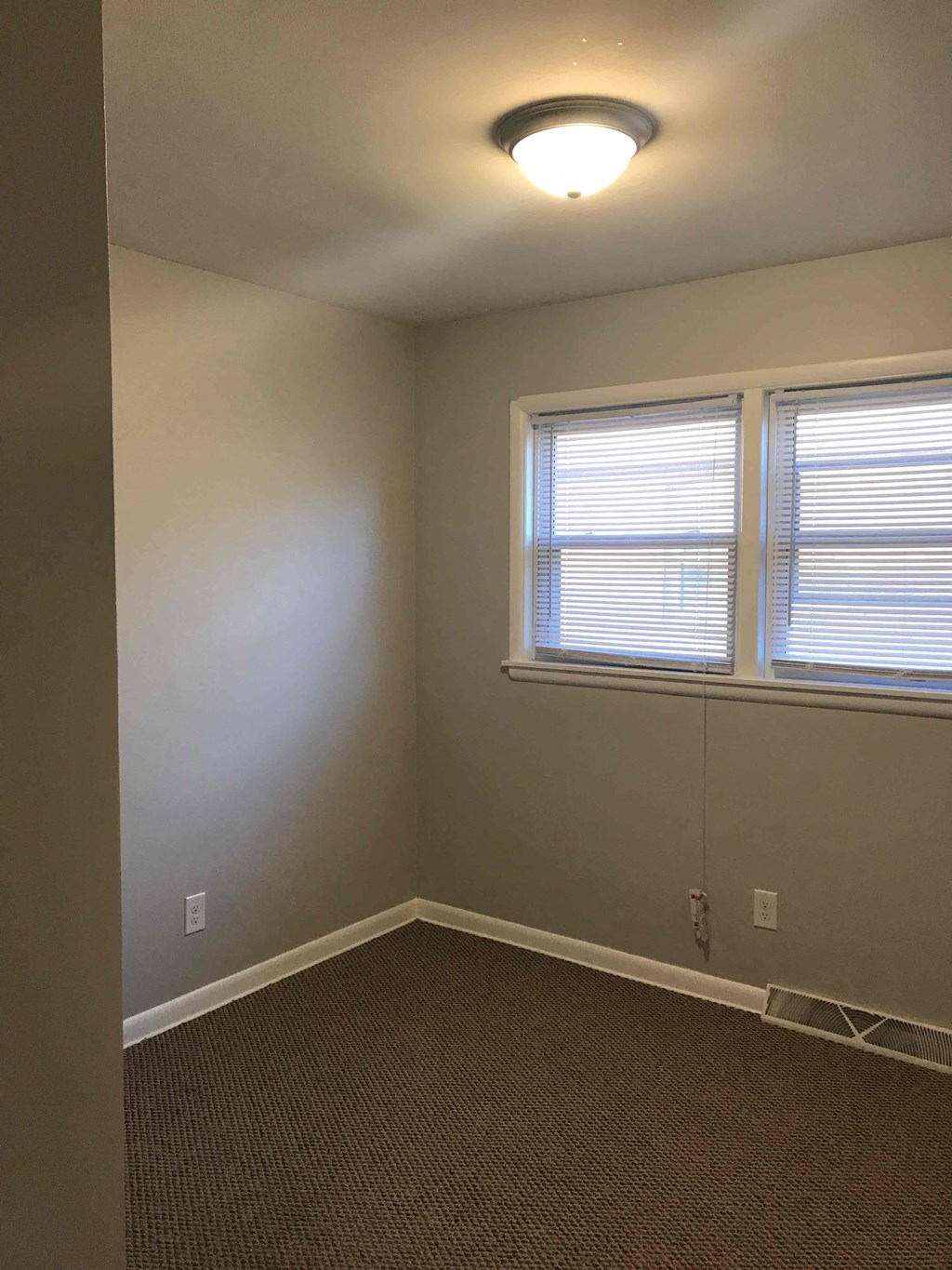an empty room with a lamp on the ceiling and two windows