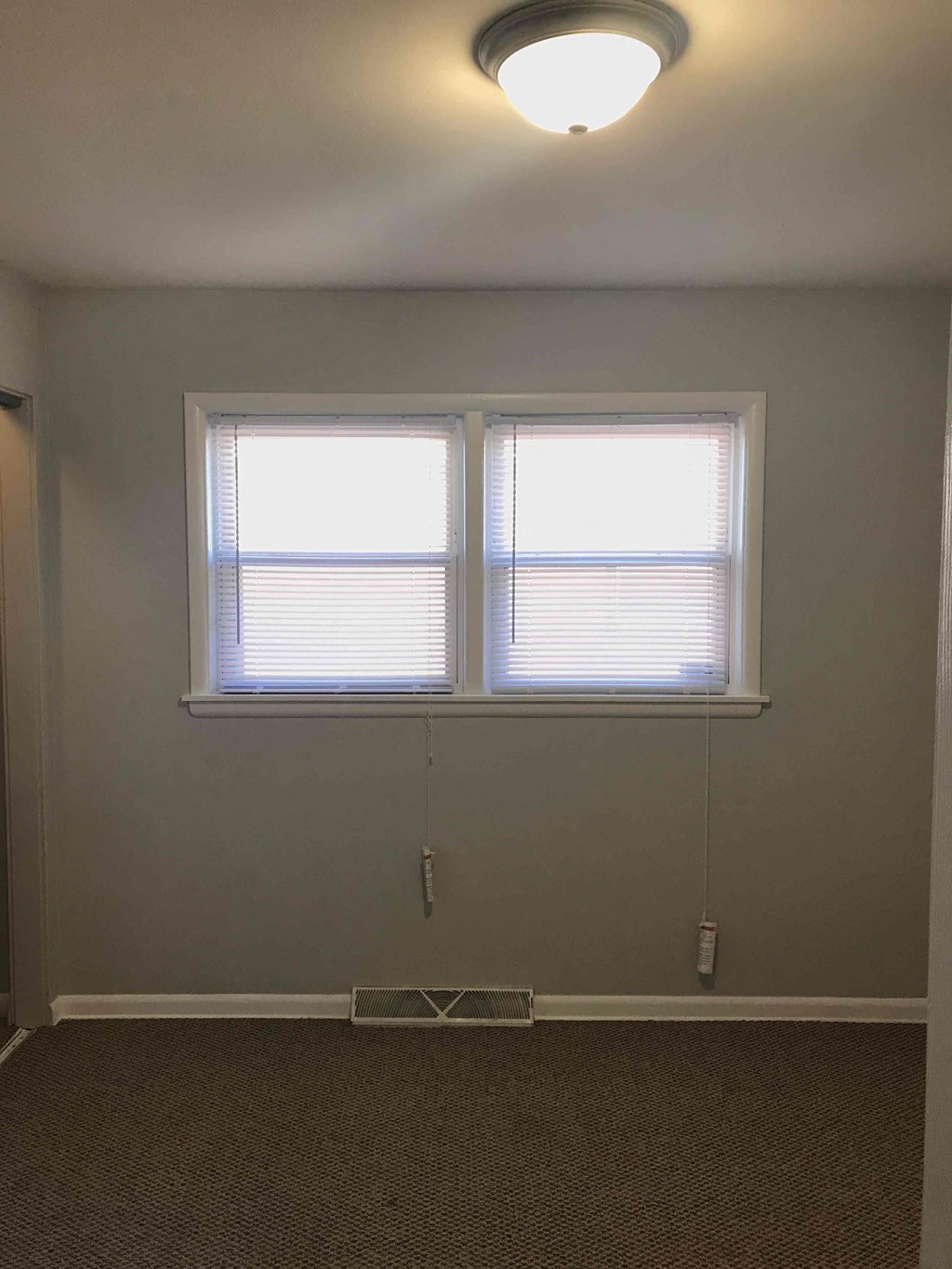 two windows in an empty room with a lamp on the ceiling