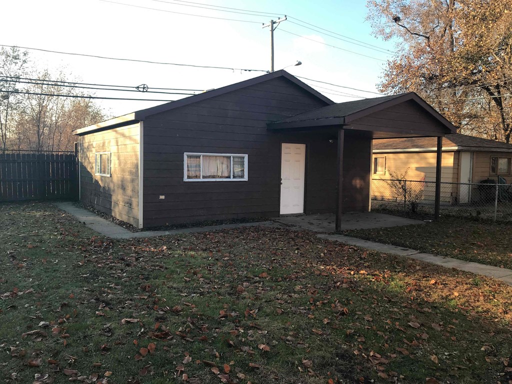 a small black house with a white door and a fenced in yard