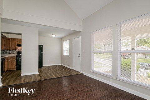 the living room of an apartment with wood flooring and large windows